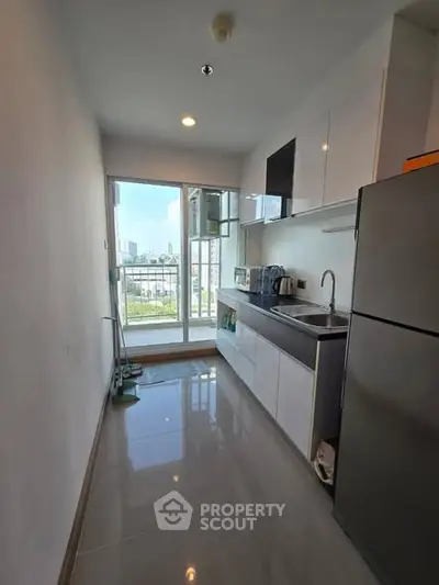 Modern kitchen with sleek cabinets and stainless steel appliances, featuring a bright view through large windows.