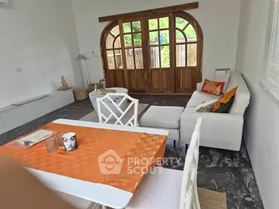 Charming living room with elegant decor and large wooden doors opening to a lush garden view.