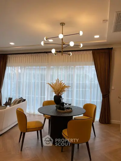 Elegant living room with modern chandelier and stylish dining area, featuring floor-to-ceiling windows and chic decor.