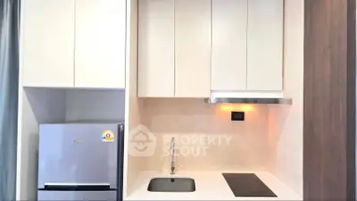 Modern kitchen with sleek cabinetry, built-in stove, and compact fridge in a stylish apartment.