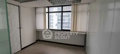 Spacious office room with large window and modern design in a high-rise building.