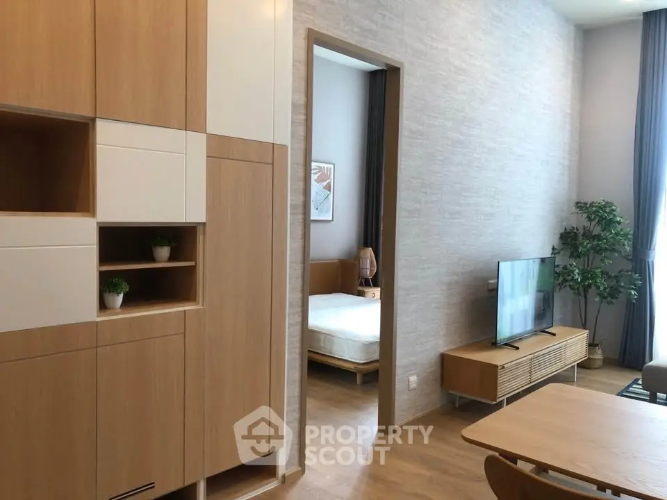 Modern living room with wooden furniture and view into a cozy bedroom