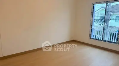 Spacious empty room with wooden flooring and large window offering natural light.