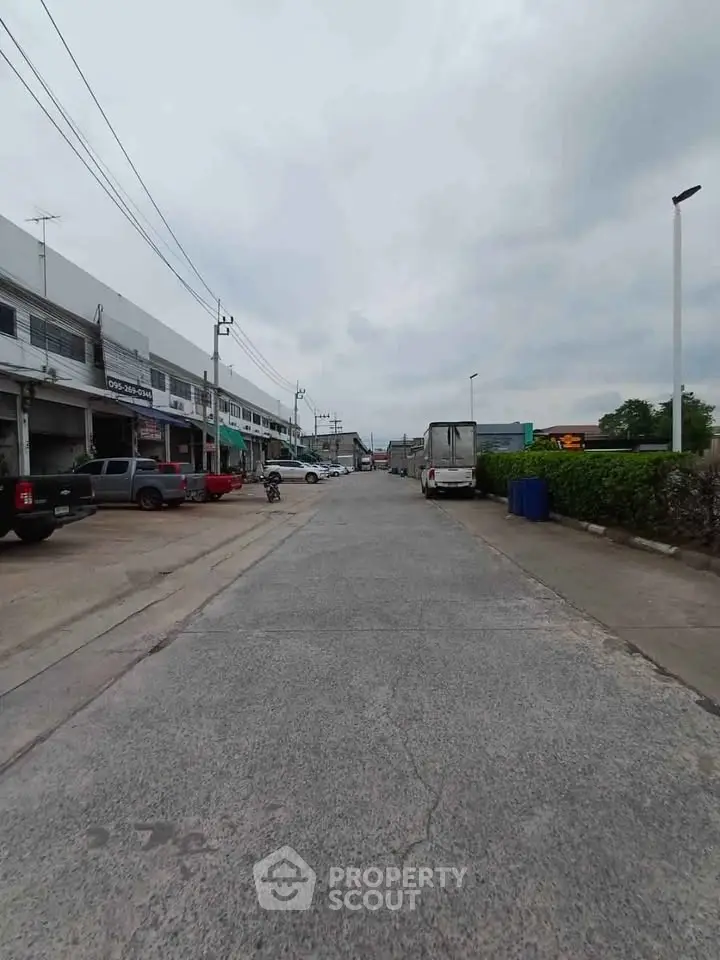 Commercial street view with shops and parked vehicles on a cloudy day.