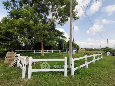 Spacious green land with white fence and lush trees, ideal for development.