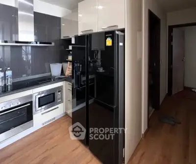 Modern kitchen with sleek black fridge and built-in appliances in stylish apartment.
