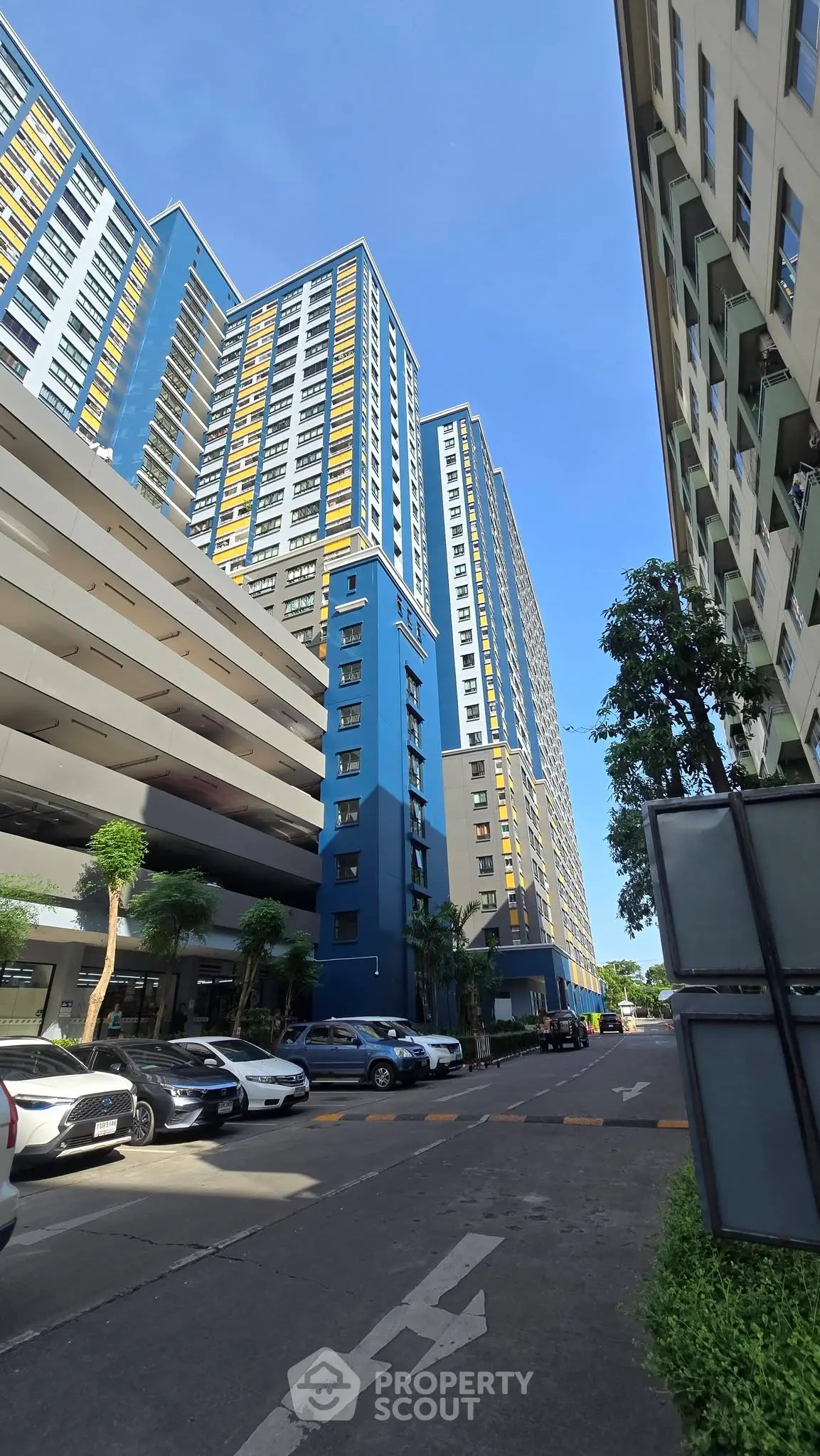 Modern high-rise residential building with parking area and lush greenery.