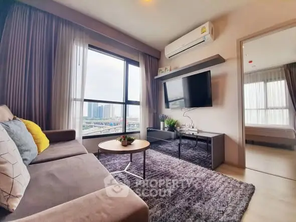 Modern living room with large window and city view, featuring cozy sofa and wall-mounted TV.