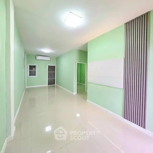 Spacious modern living room with green walls and sleek tile flooring, perfect for contemporary living.