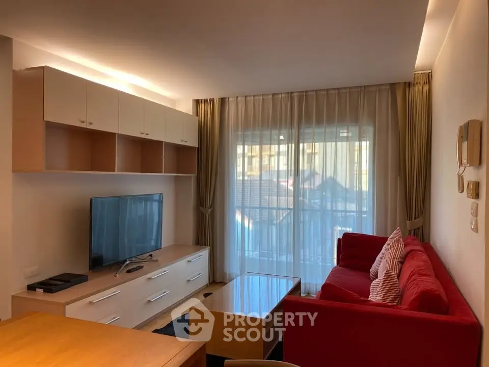 Modern living room with red sofa, TV, and large window with sheer curtains.