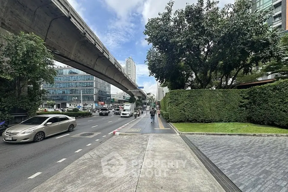Urban street view with modern buildings and elevated train tracks, showcasing city living and transportation.