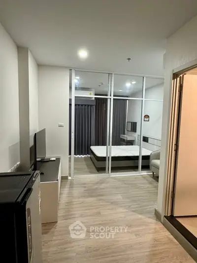 Modern studio apartment with glass partition, wood flooring, and sleek furnishings.