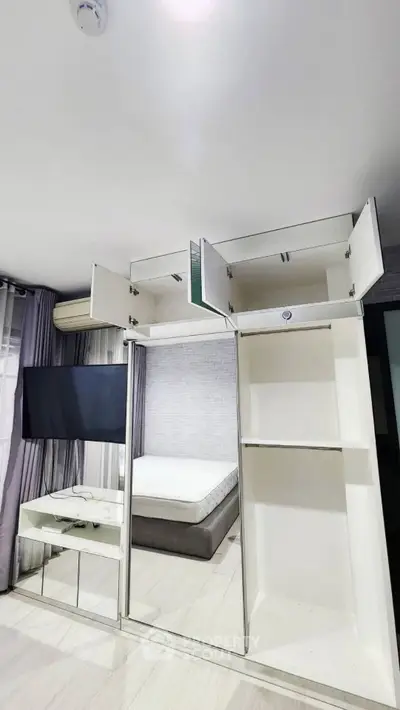 Modern bedroom with sleek storage solutions and wall-mounted TV, featuring a minimalist design and ample natural light.