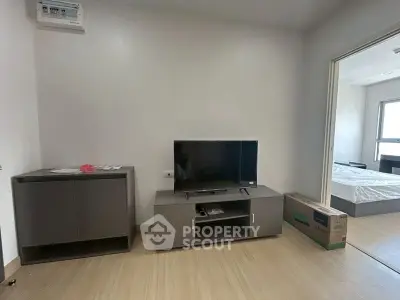 Modern living room with sleek TV stand and flat-screen TV, adjacent to a cozy bedroom.