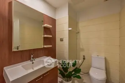 Modern bathroom with sleek sink and toilet, featuring elegant wooden accents and a potted plant.