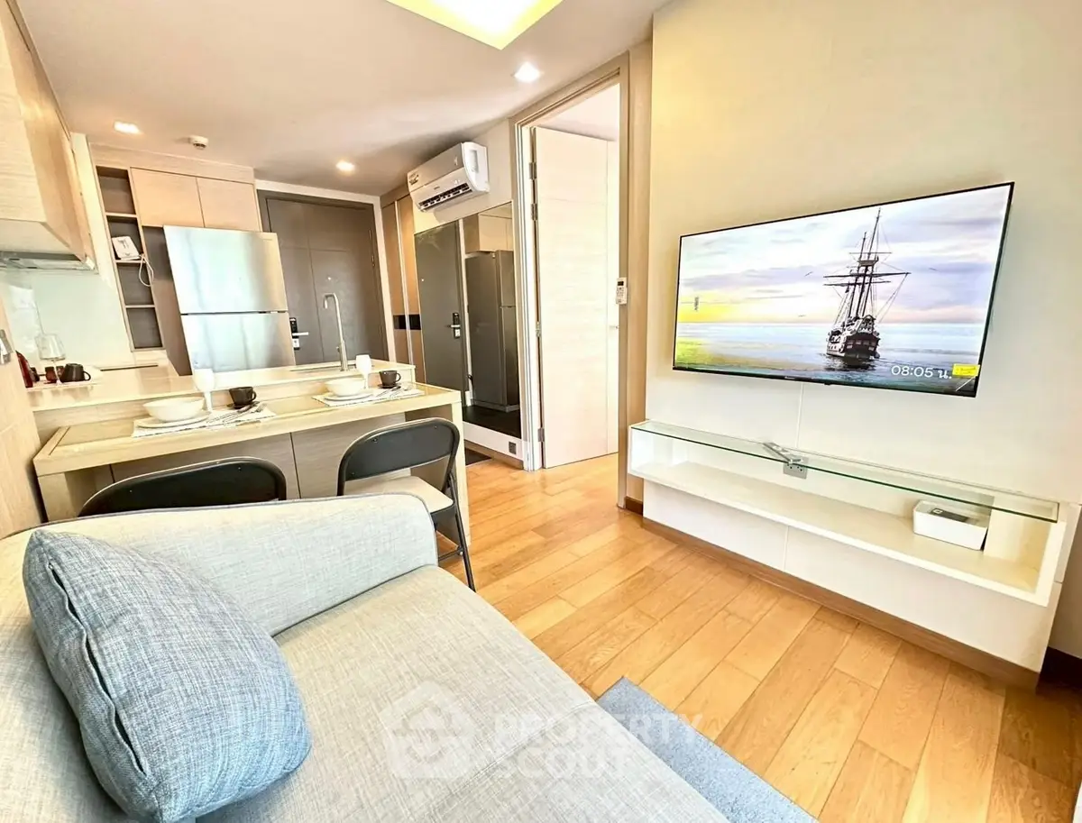 Modern living room with open kitchen, featuring sleek furniture and a wall-mounted TV, perfect for urban living.