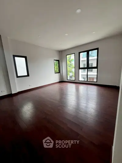 Spacious empty room with dark wood flooring and large windows offering natural light.