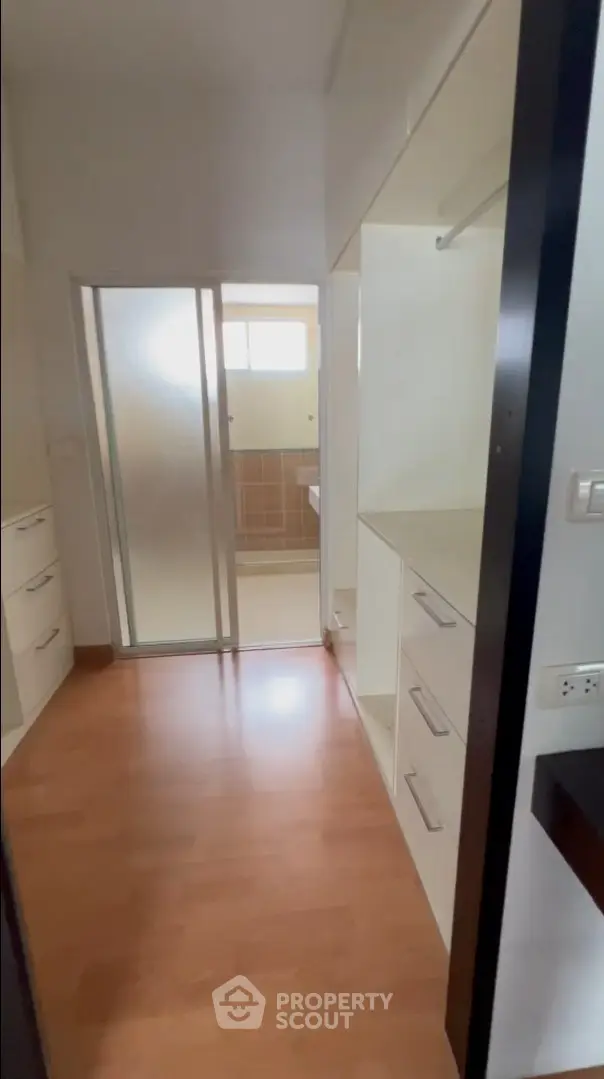 Spacious walk-in closet with wooden flooring and sliding door leading to bathroom.