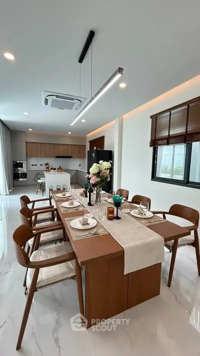 Elegant dining area with modern kitchen, featuring sleek wooden furniture and stylish lighting.