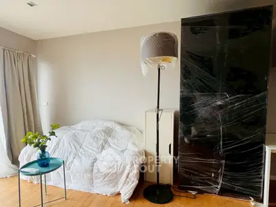 Cozy bedroom with modern decor and natural light, featuring a stylish floor lamp and compact furniture.