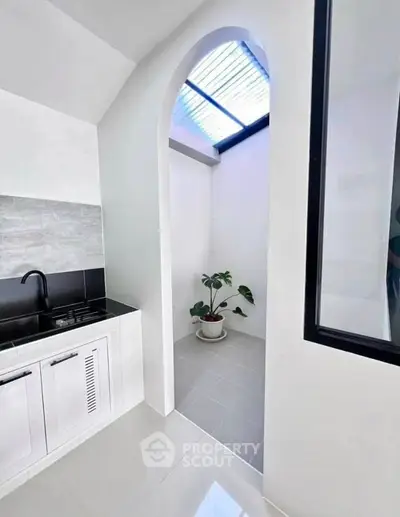 Modern kitchen with sleek design and archway leading to a bright patio area.