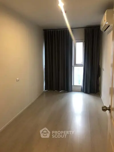 Spacious bedroom with wooden flooring and large window, perfect for natural light.