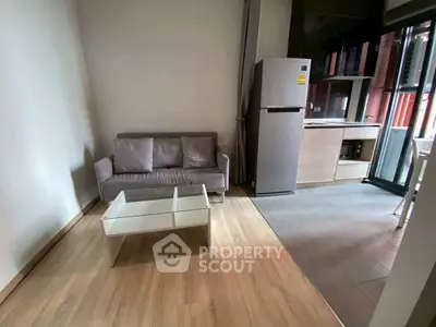 Modern living room with sleek sofa and glass coffee table, adjacent to a compact kitchen area.