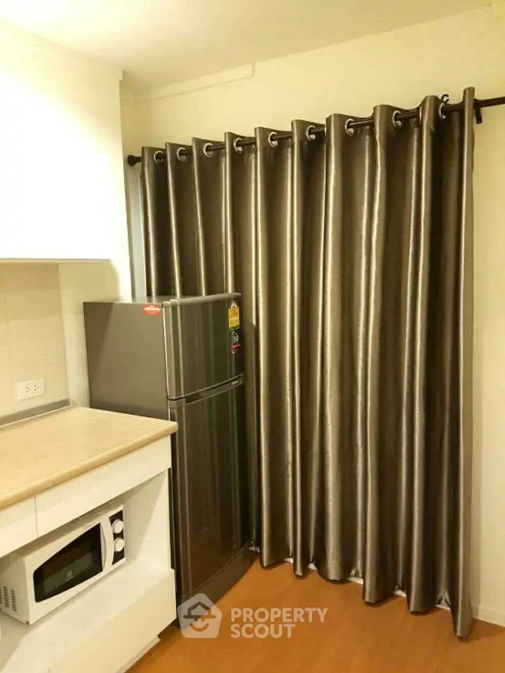 Modern kitchen with sleek fridge and microwave, featuring elegant floor-to-ceiling curtains.