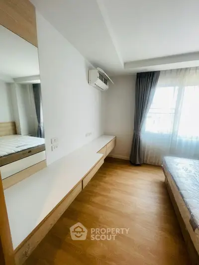 Modern bedroom with wooden flooring and large window, featuring a built-in desk and air conditioning.
