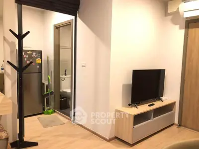 Modern apartment interior with TV, fridge, and bathroom entrance, showcasing compact living space.