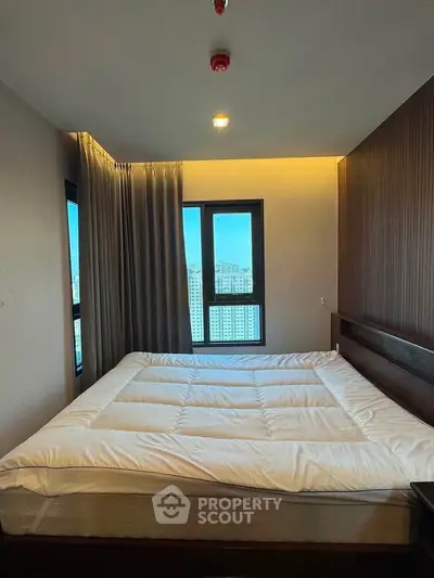 Modern bedroom with large windows and city view, featuring cozy bedding and elegant design.