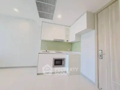 Modern minimalist kitchen with sleek white cabinets and built-in microwave in a bright apartment.
