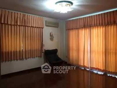 Spacious living room with elegant curtains and cozy armchair, featuring warm lighting and polished wooden floors.