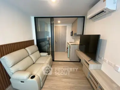Modern living room with sleek furniture and integrated kitchen area, featuring a cozy sofa and large TV.