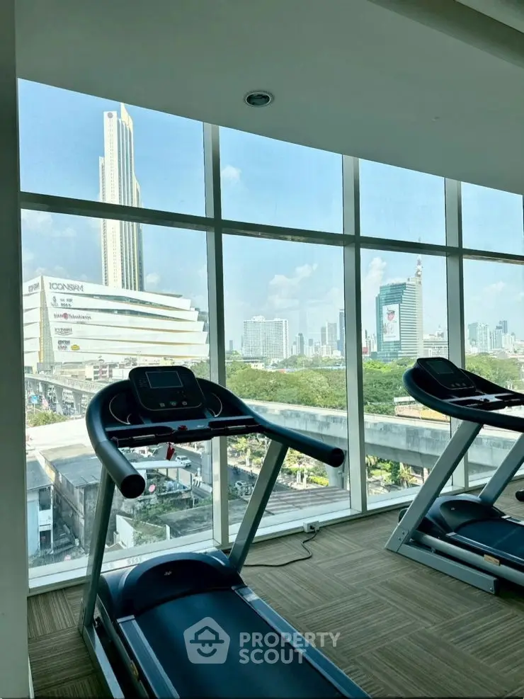 Modern gym with city view from large windows, featuring treadmills and skyline.