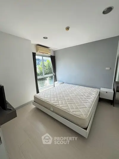 Spacious bedroom with large window and modern furnishings in a bright apartment.