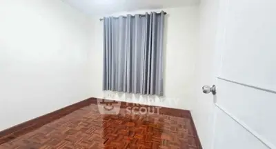Spacious empty room with polished wooden floors and elegant gray curtains.