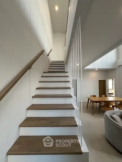 Modern interior with elegant staircase and spacious living area, featuring stylish furniture and open layout.