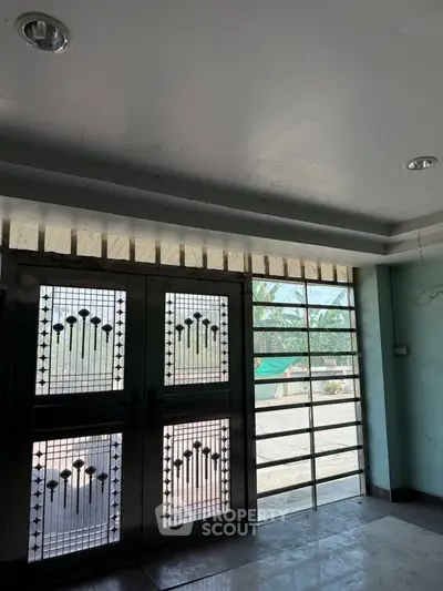 Spacious entrance with decorative metal doors and large windows offering natural light.