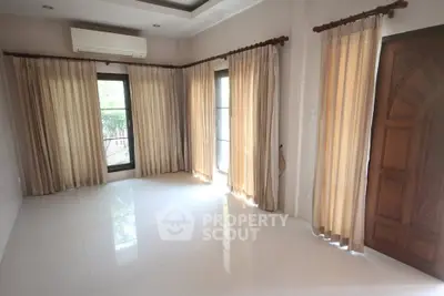 Spacious living room with large windows and elegant curtains, featuring a wooden door and air conditioning.