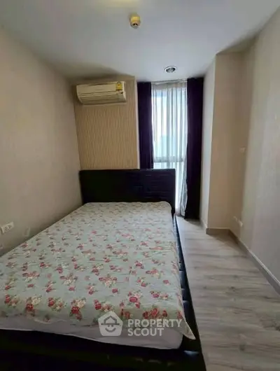 Cozy bedroom with floral bedding and natural light from a large window, featuring modern air conditioning.
