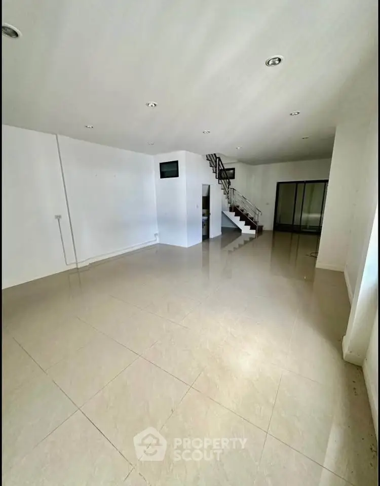 Spacious open-plan living area with modern staircase and large windows.