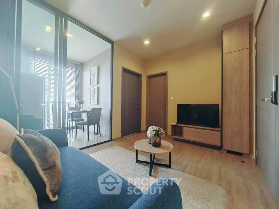 Modern living room with blue sofa and TV, adjacent to a dining area with glass partition.