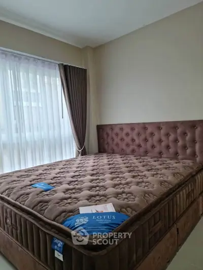 Spacious bedroom with plush brown bed and large window with curtains.