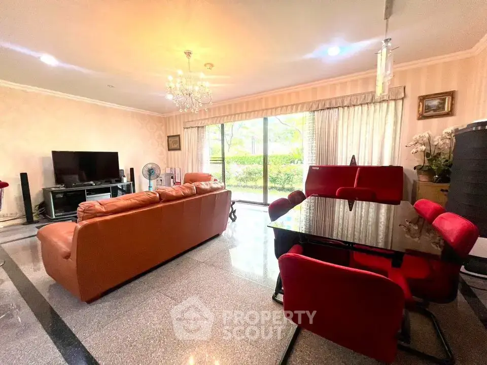 Spacious living room with elegant chandelier and garden view, featuring modern furniture and large windows.