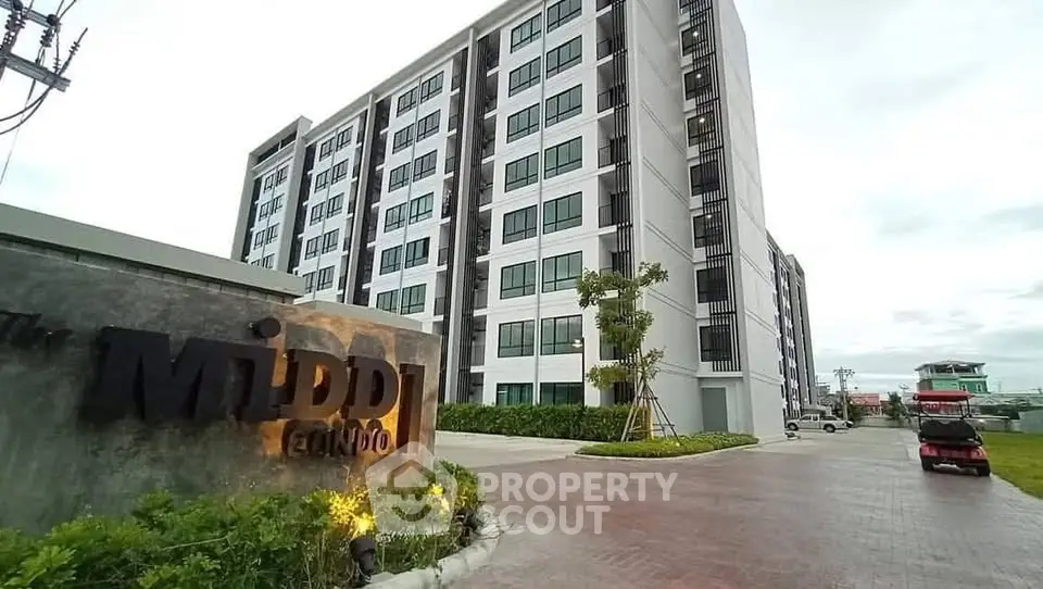 Modern apartment building with landscaped entrance and ample parking space.