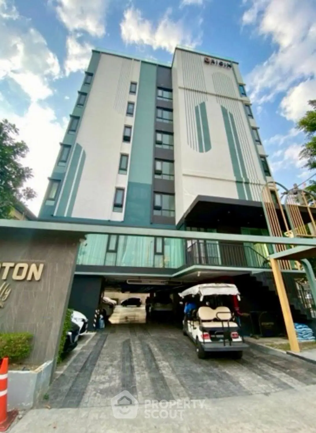 Modern multi-story building with sleek design and spacious parking area under a clear blue sky.