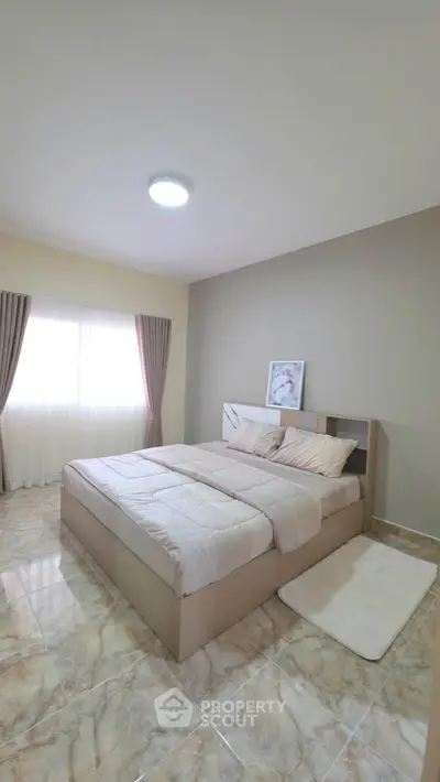 Spacious bedroom with modern decor and natural light, featuring a comfortable bed and elegant curtains.