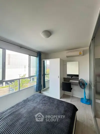 Modern bedroom with large windows, stylish decor, and ample natural light in urban apartment.