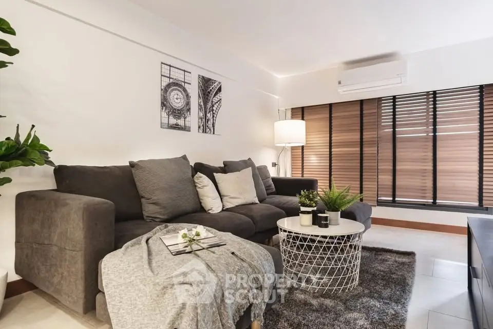 Stylish modern living room with cozy gray sofa, chic decor, and large windows with blinds.